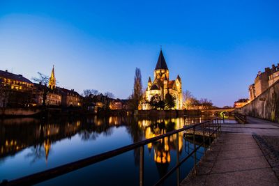 Illuminated buildings by river against sky at dusk