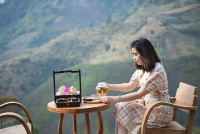 Side view of woman sitting on table against mountain