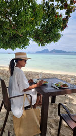 Rear view of woman sitting on chair at beach