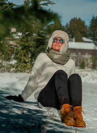 Young woman sitting on snow covered tree