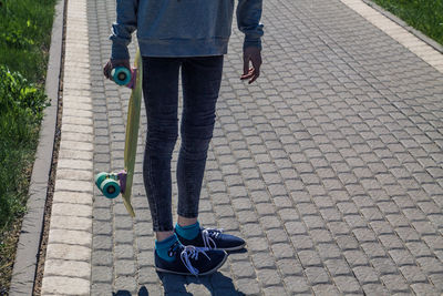 Low section of woman with skateboard standing on footpath