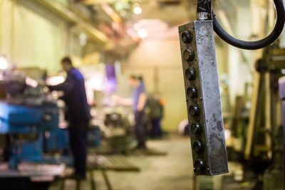 Shop crane control panel box with blurry milling workers in the background