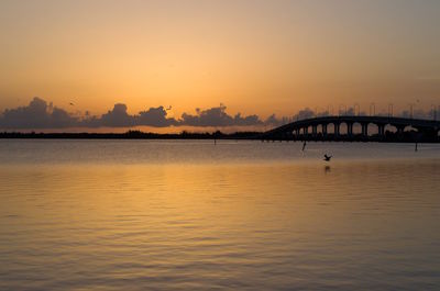 Silhouette bridge over sea against sky during sunset