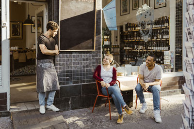 Customers talking to male owner standing by store doorway