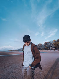 Man with hands in pockets standing at beach against sky