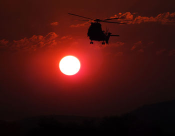 Silhouette helicopter flying against sky during sunset