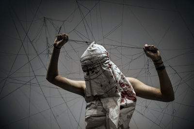 Woman tangled in strings covered with blood stained fabric standing against gray background