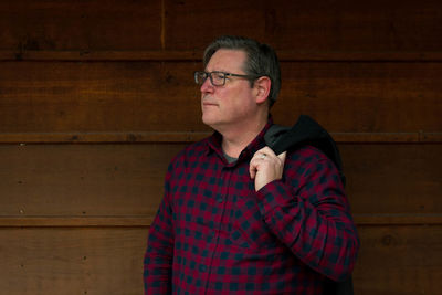 Mature man looking away while standing against wall