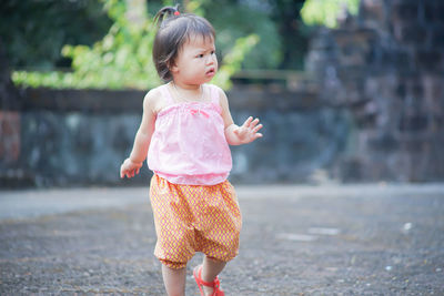 Cute baby girl looking away while walking on footpath