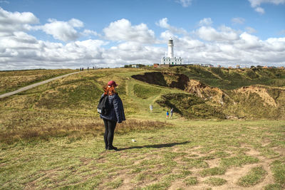 A figure watching over the sea on top of a cliff with a lighthouse. 