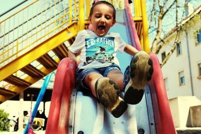 Low angle view portrait of happy boy sitting outdoors