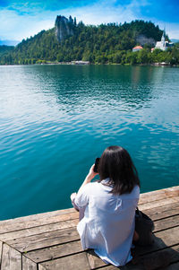 Rear view of woman sitting on pier against lake