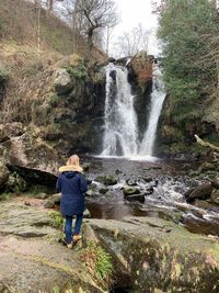 Rear view of woman standing on rock against waterfall