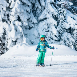 Full length portrait of boy skiing against snow covered pine trees