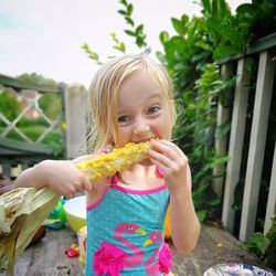 Portrait of girl eating corn while standing against plants