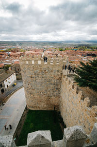 People at walls of avila against cloudy sky