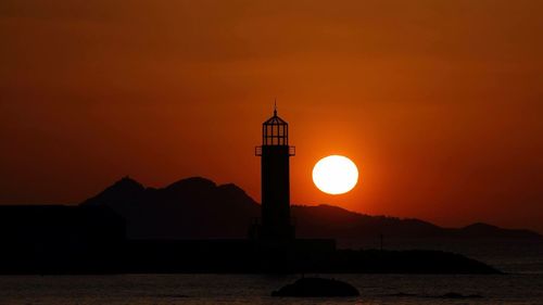 Silhouette lighthouse by sea against sky during sunset