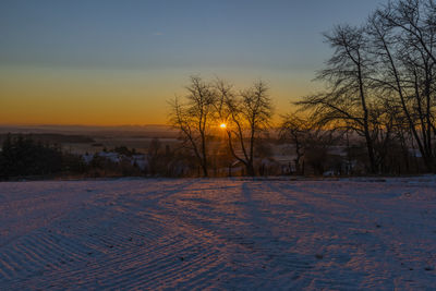 Snow covered field against sky during sunset