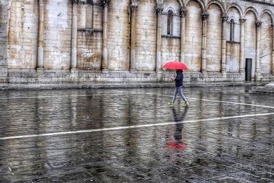 Man walking with umbrella on wet street against building