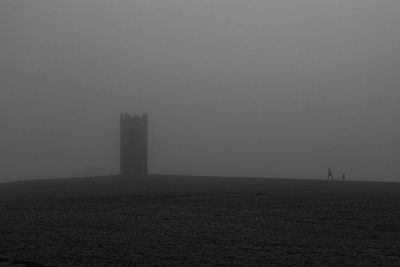 Silhouette building on field against sky during foggy weather