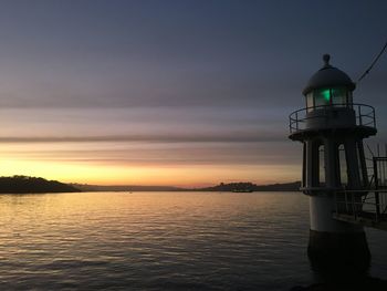 Lighthouse in sea against sky during sunset