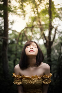 Close-up of young woman with eyes closed standing against tree