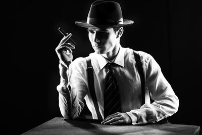 Young man wearing suspenders holding cigar against black background