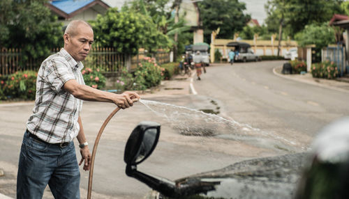 Man washing car from hose on street