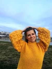 Portrait of smiling young woman in sweater against sky