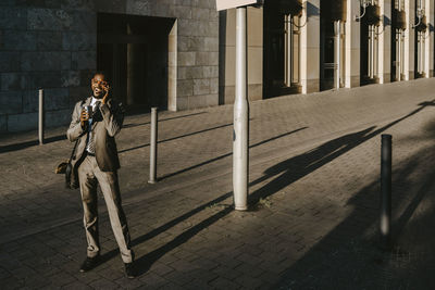 Male entrepreneur talking on smart phone while standing on footpath during sunny day