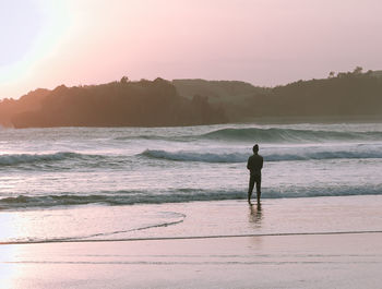 Rear view of man standing at beach during sunset