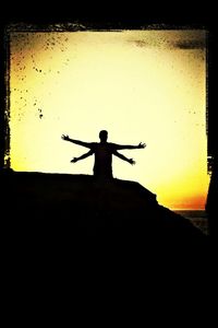 Rear view of silhouette person standing on cross against sky during sunset