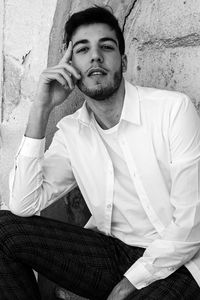 Portrait of young man sitting against wall