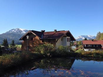 Houses by lake and buildings against clear blue sky