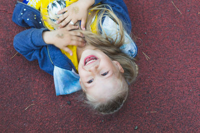 Happy caucasian girl with long hair lies on the playground, hugs her hands to her chest and laughs 