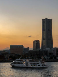 Nautical vessel on sea by buildings against sky during sunset