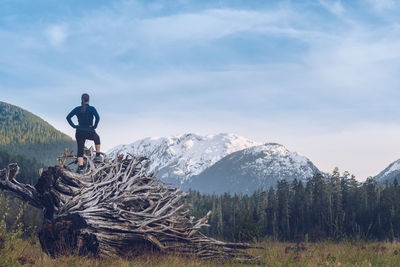 Rear view of woman standing on log at forest against cloudy sky