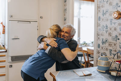 Smiling senior man embracing female caregiver at home