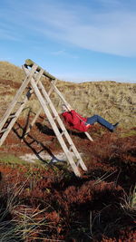 Side view of senior man playing on swing against sky