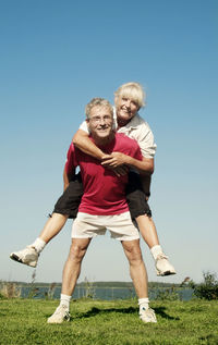 Senior man piggybacking woman against clear sky