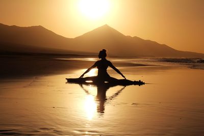 Silhouette woman on shore against sky during sunset