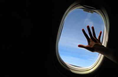 Close-up of hand against sky seen through airplane window