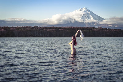 Side view of topless young woman standing in lake against sky during sunset