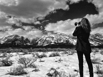 Rear view of woman photographing cloudy sky over snowcapped mountain