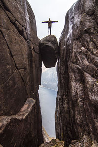 Low angle view of person standing on rock with arms outstretched