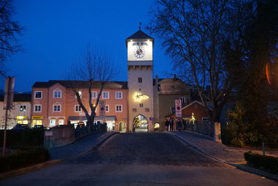 Illuminated street amidst buildings against sky at night