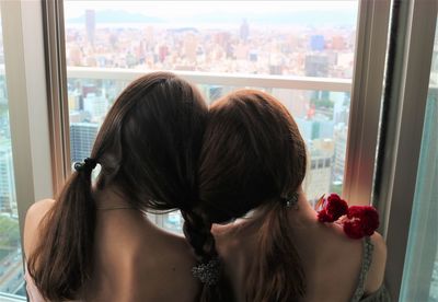 Rear view of sisters with braided hair against window