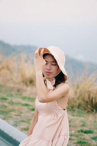 Young woman wearing hat standing on field against sky