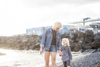 Mother and son standing at beach against sky