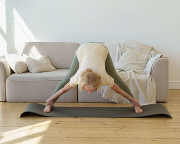 Active healthy senior woman standing in downward facing dog yoga pose while practicing yoga at home